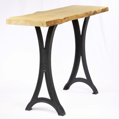 Live edge wood console table supported by black cast iron pedestal legs, minimalist studio setting