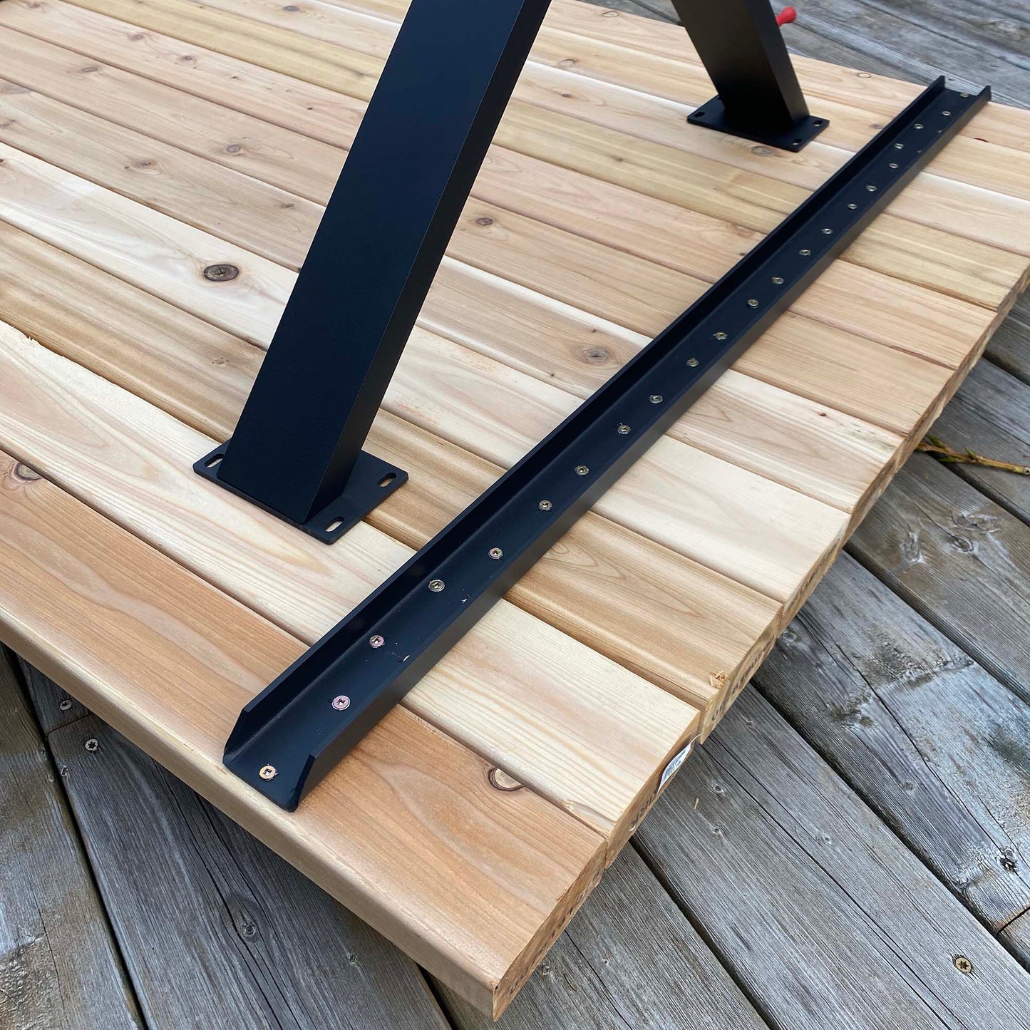 Black aluminum metal table cleat placed on a wooden surface with a part of a black metal table leg in the background.